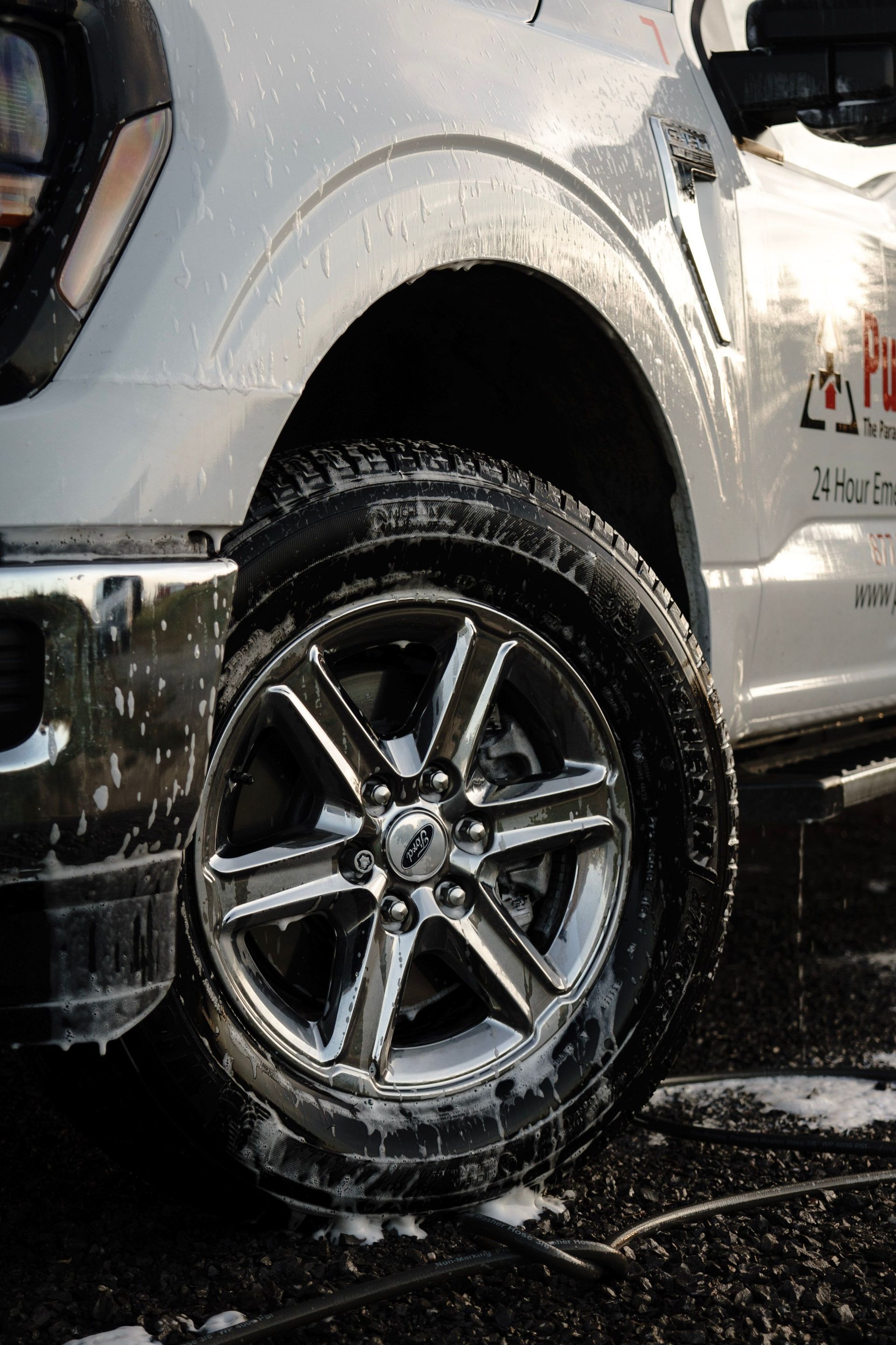 Close-up of a shiny car wheel being washed on a gravel surface outdoors.