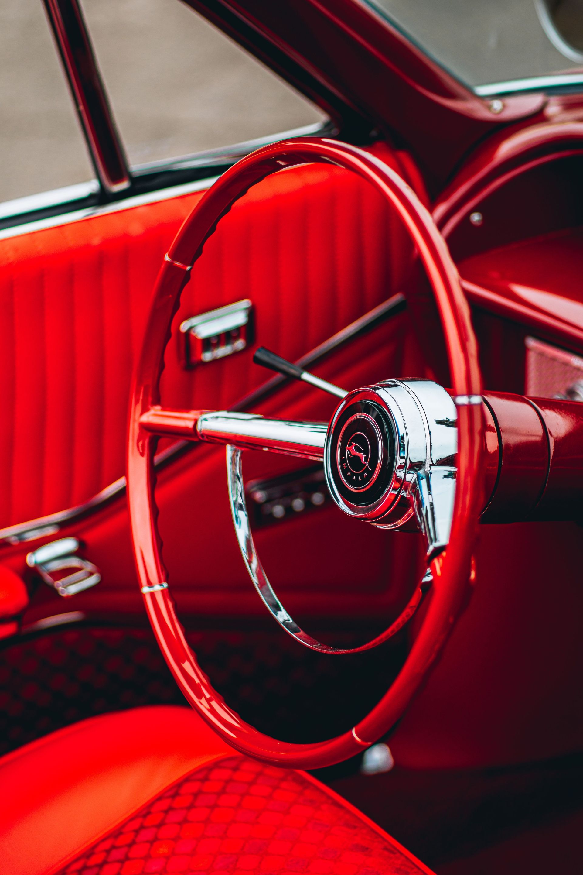 Close-up of a vintage car's red steering wheel and interior chrome elements.