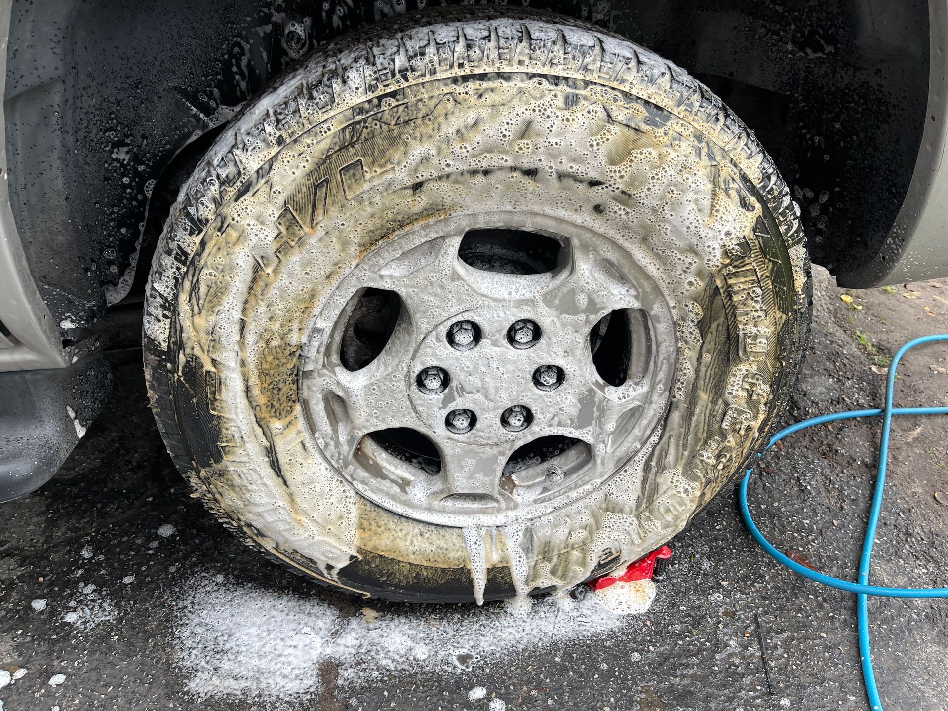 Close-up of a car wheel being cleaned with soap during a detailed car wash.